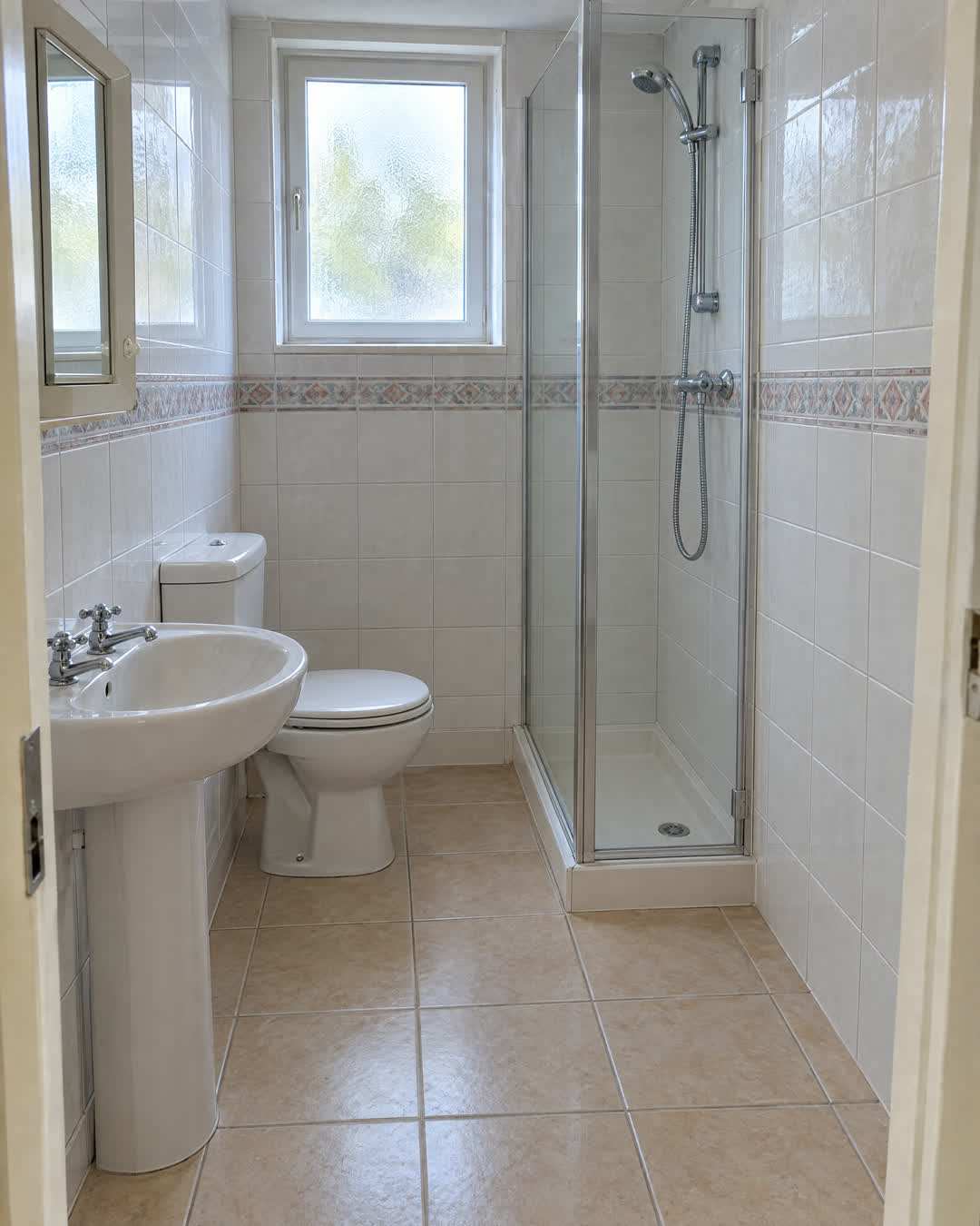 Voor: badkamer uit de jaren negentig met tegelwerk, douchecabine, toilet en wastafel