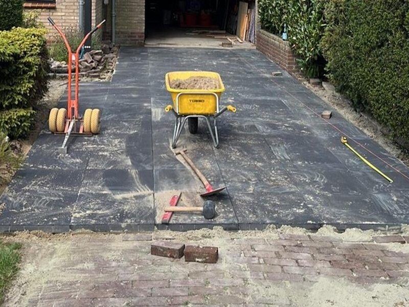 Oprit in voorbereiding voor nieuwe bestrating, met kruiwagen en gereedschap