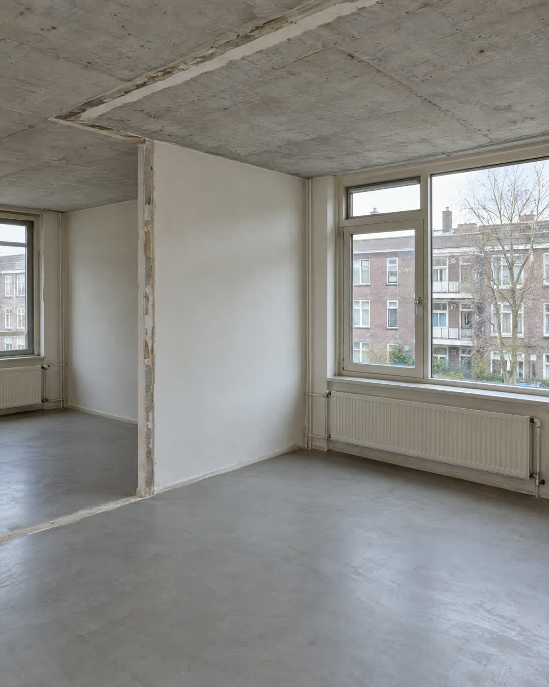 Na: dezelfde ruimte na binnensloop, met tussenwand en plafond weg en kozijn en radiator behouden