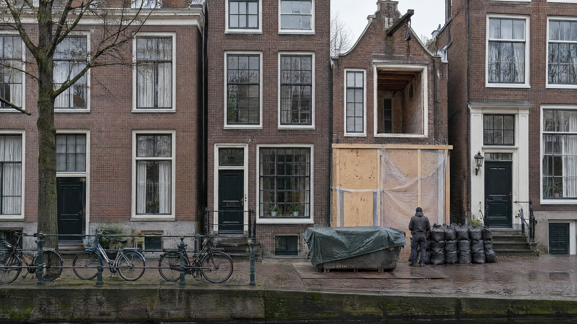 Amsterdams grachtenpand dat wordt voorbereid op stripwerk, met een afgedekte container