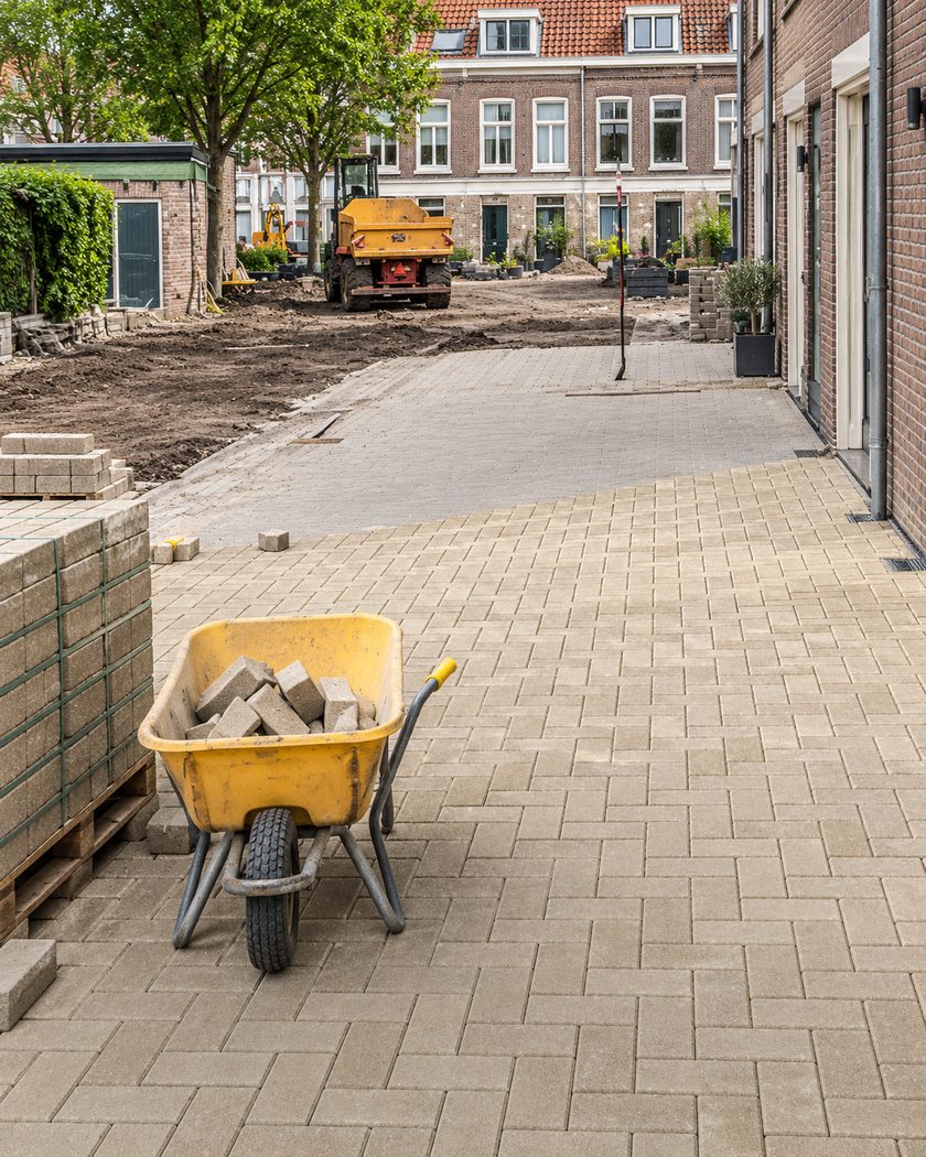 Nieuw gelegde gele klinkers in een woonstraat, met een kruiwagen stenen en pallets klinkers