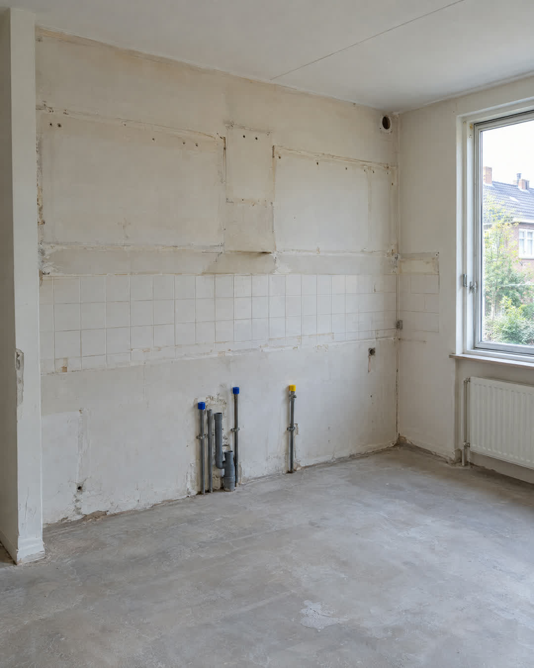 Na: dezelfde keukenwand leeg, met afgedopte water- en gasleidingen