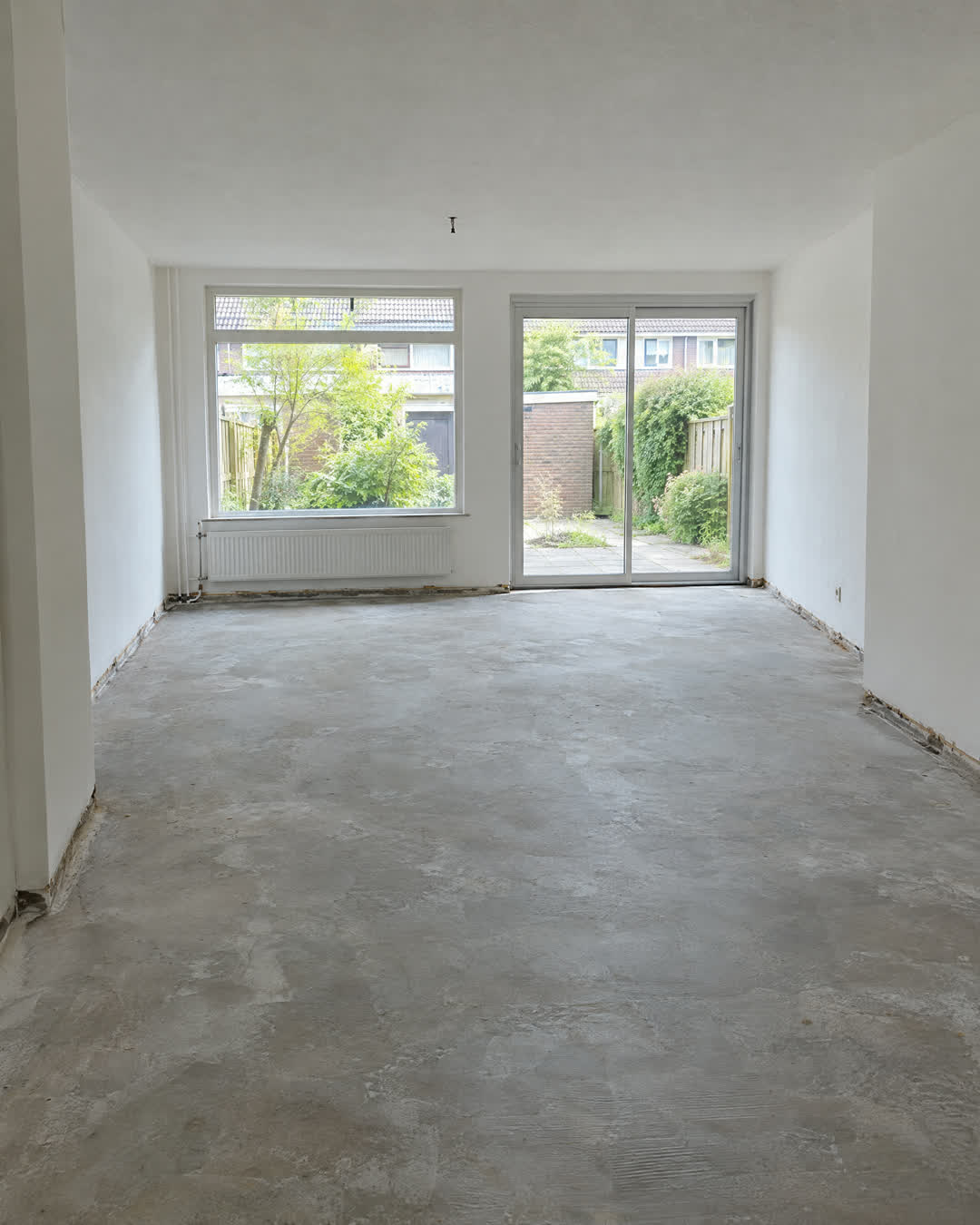 Na: dezelfde woonkamer met kale betonvloer, laminaat en plinten verwijderd