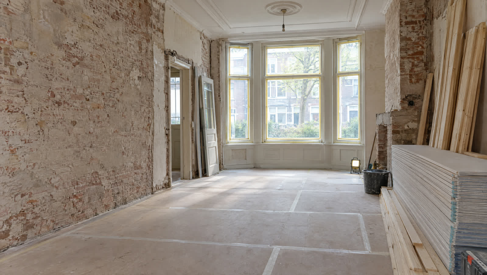 Woonkamer van een jaren-dertigwoning in de sloopfase, met kaal metselwerk en klaargezet bouwmateriaal
