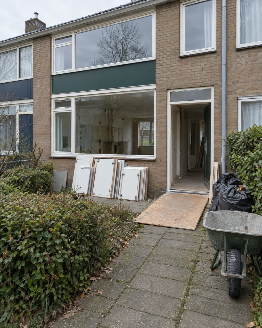 Voortuin van een rijtjeshuis met gedemonteerde keukendeurtjes, een afgeschermde drempel en puinzakken
