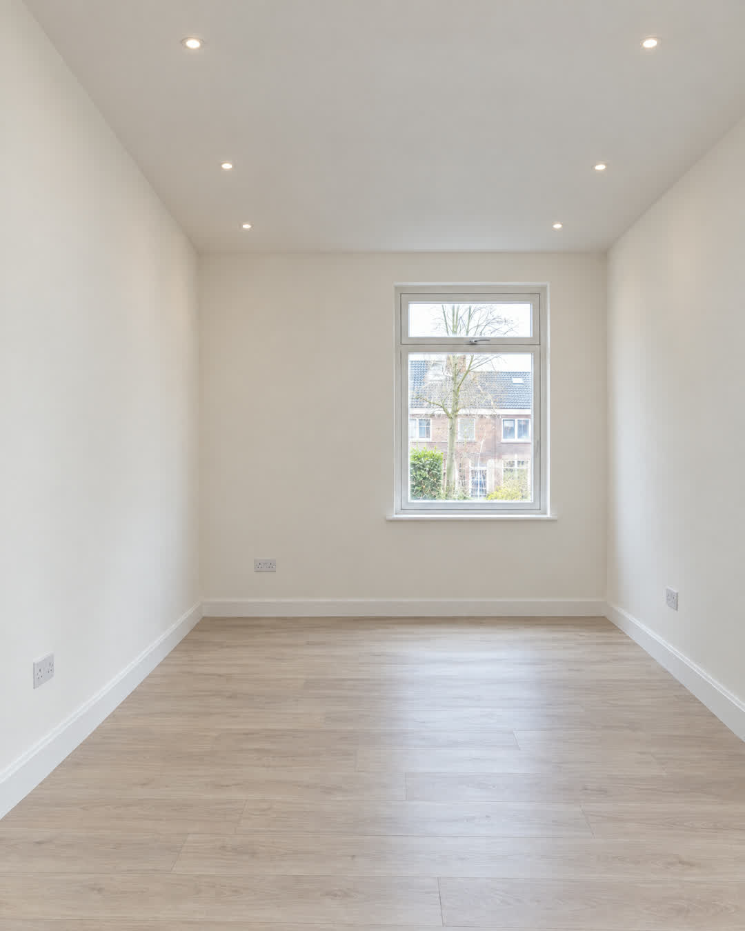 Voor: afgewerkte kamer met glad stucwerk, een plafond met spots en laminaat
