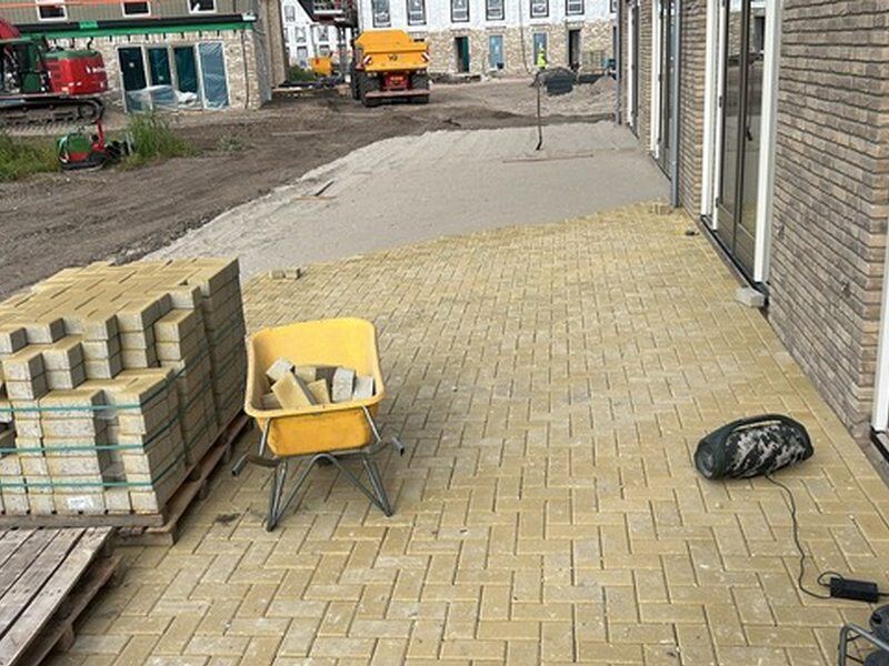 Gele klinkers worden gelegd, met pallets stenen en een kruiwagen