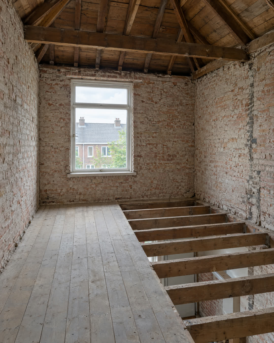 Na: dezelfde slaapkamer gestript, met kaal metselwerk, open kap en zichtbare balken